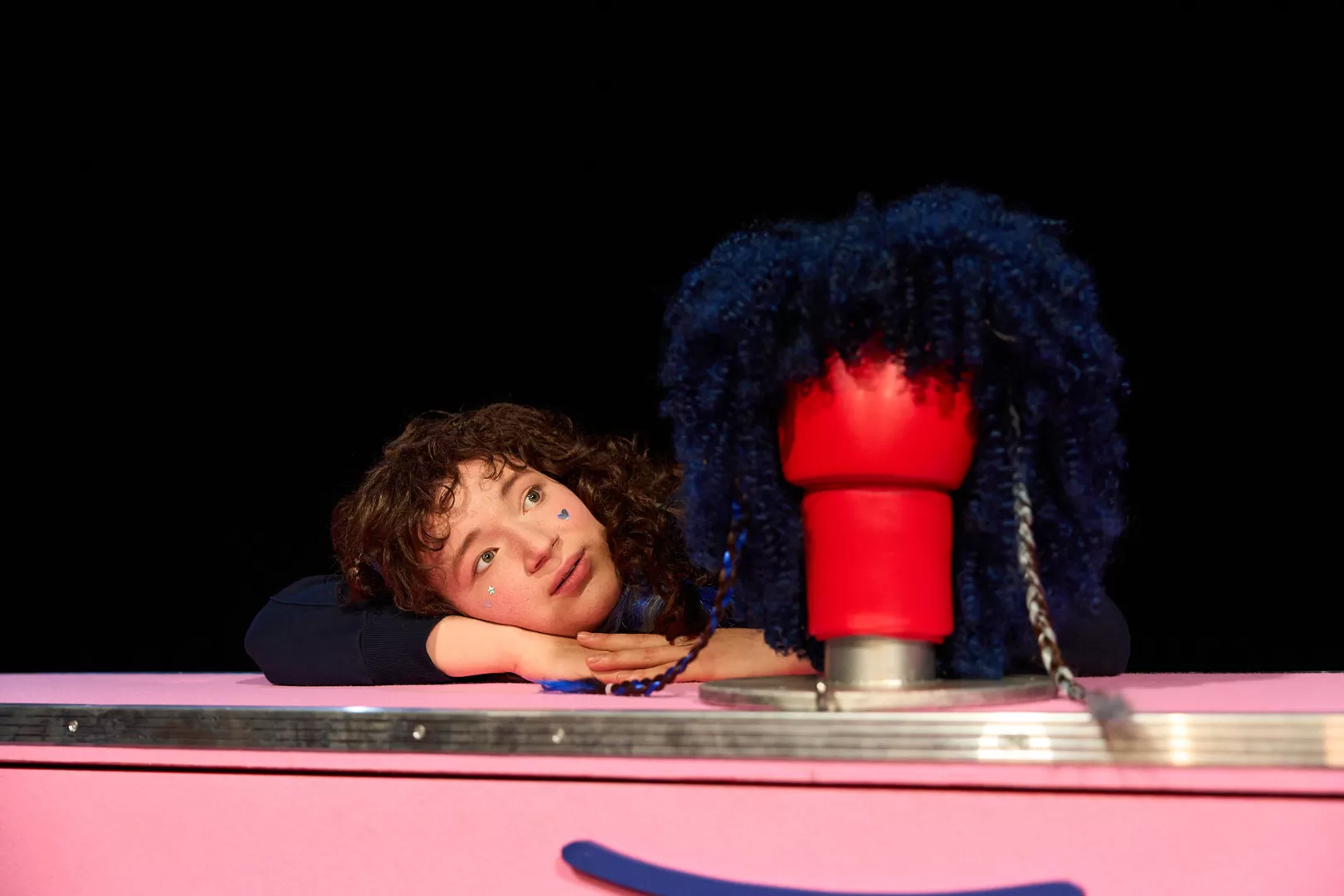EIne Person mit Locken schaut auf einen Boxhandschuh, dem eine lockige Perücke übergeworfen ist