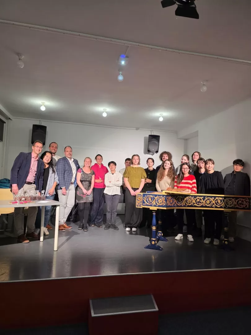 Eine Gruppe Menschen steht versammelt hinter einem Cembalo.