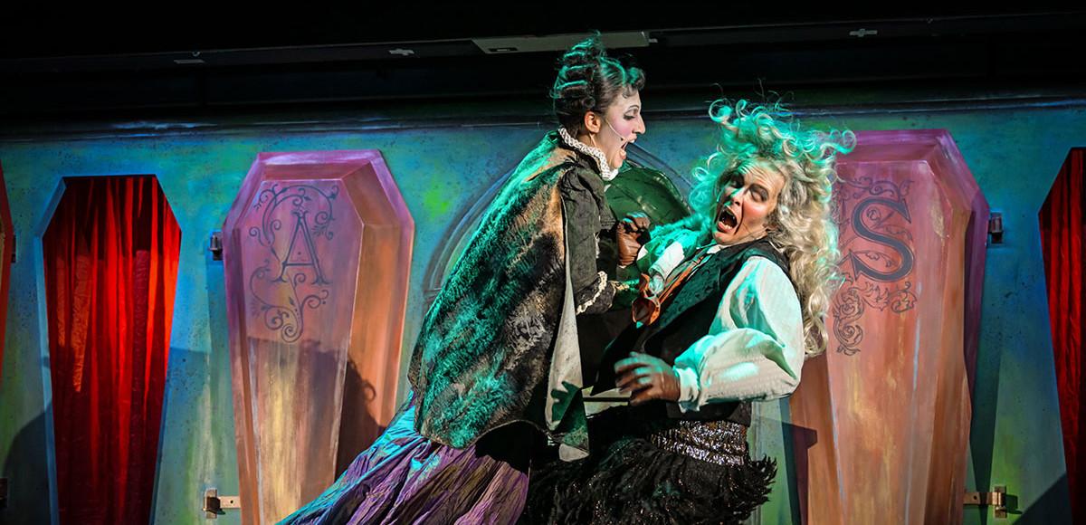 Zwei Menschen sind auf der Bühne, die eine Person springt auf die andere, erschrockene Person zu