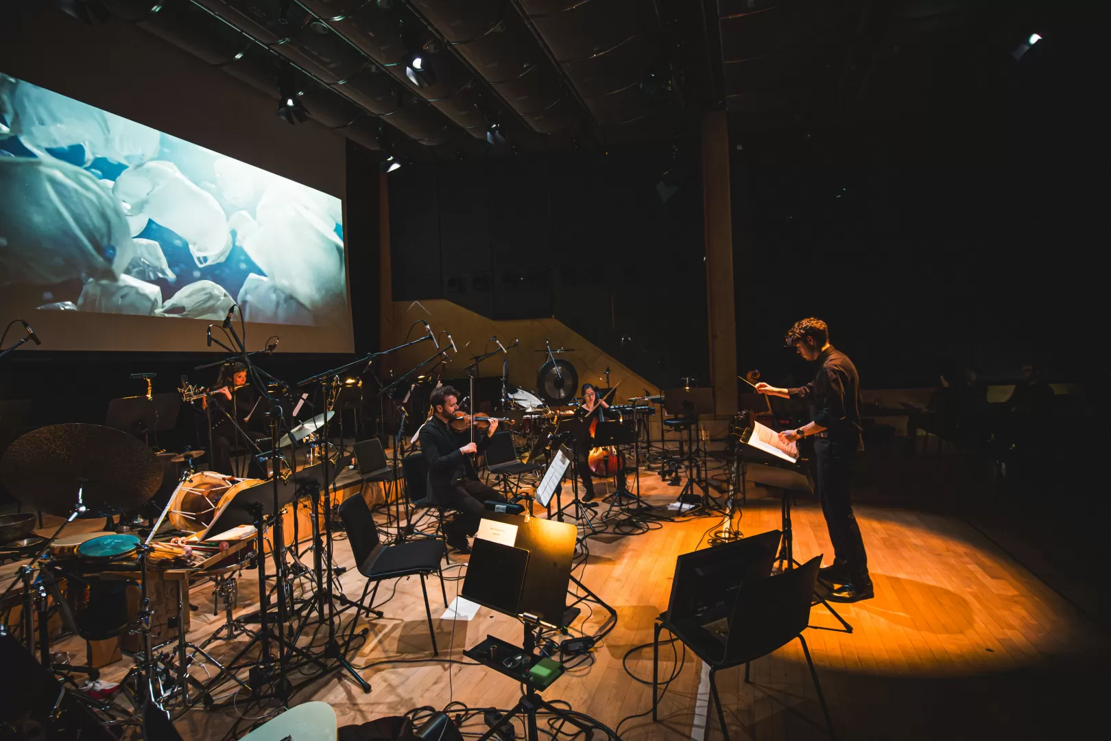 Ein Dirigent dirigiert ein Ensemble live zu einem Film, der auf der Leinwand gezeigt wird.