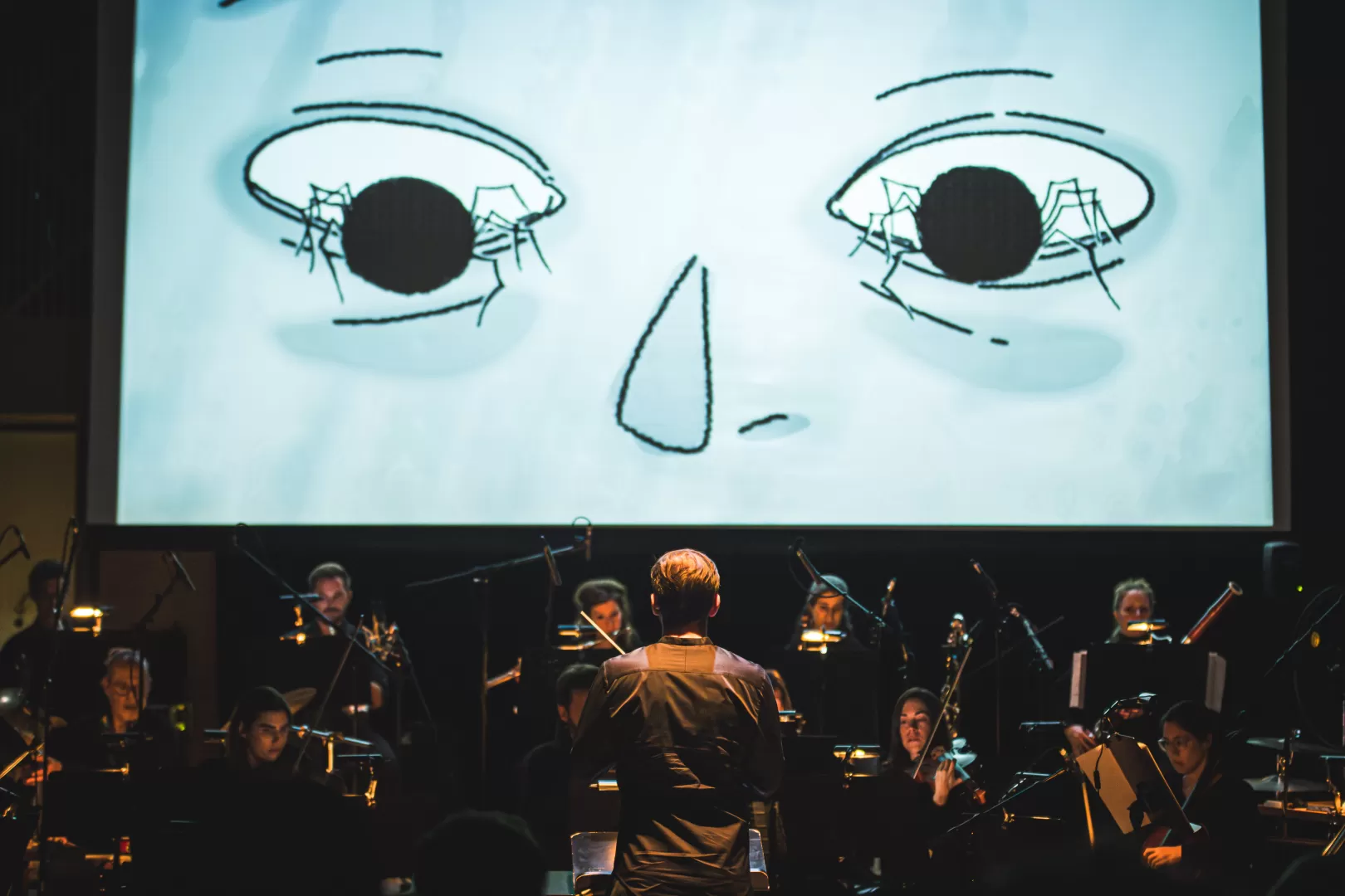 Dirigient vor einem Ensemble, im Hintergrund eine Leinwand auf der ein Stummfilm