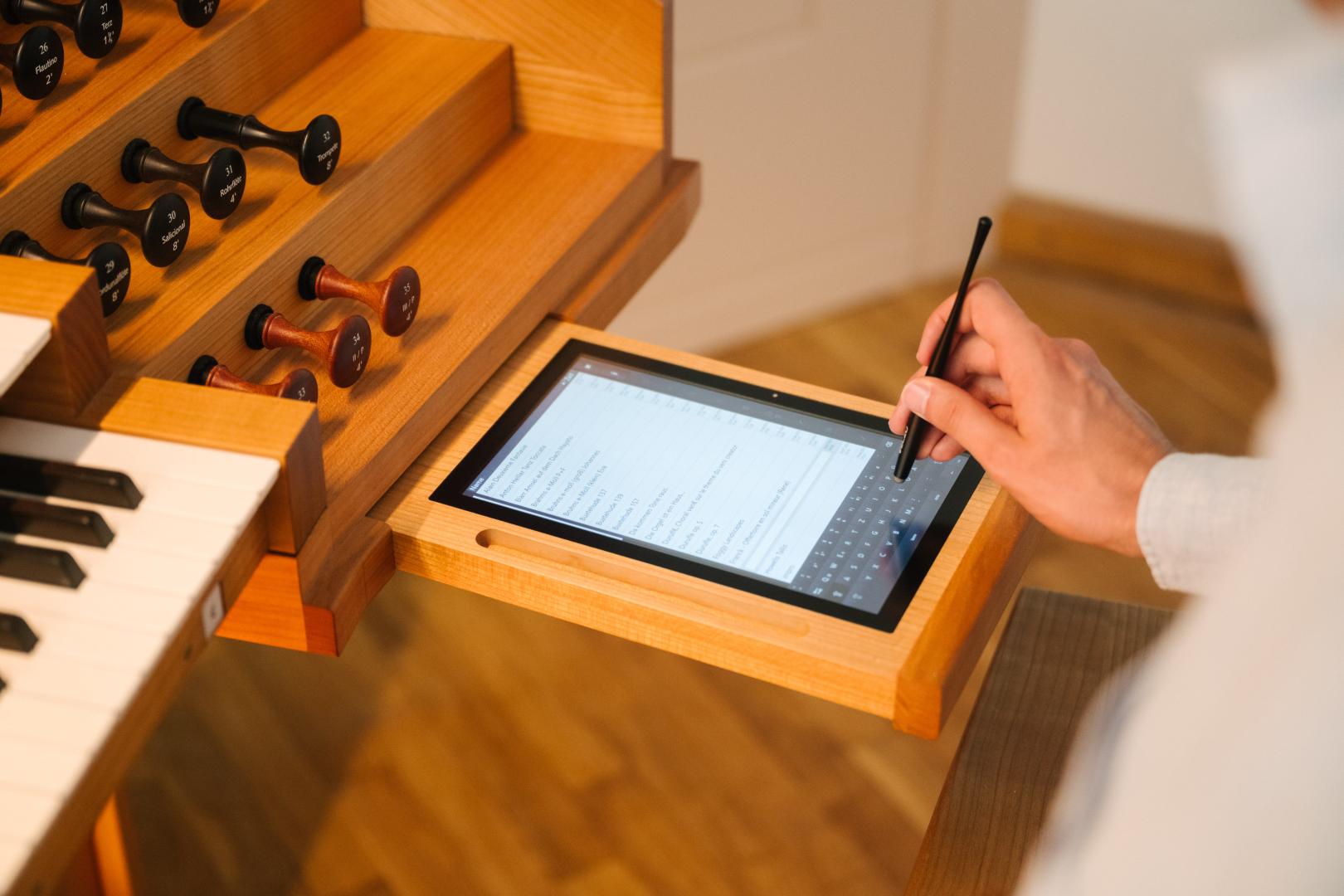 Hand einer Person, die auf dem in den Spieltisch der Rieger-Orgel integrierten Tablet etwas eingibt.