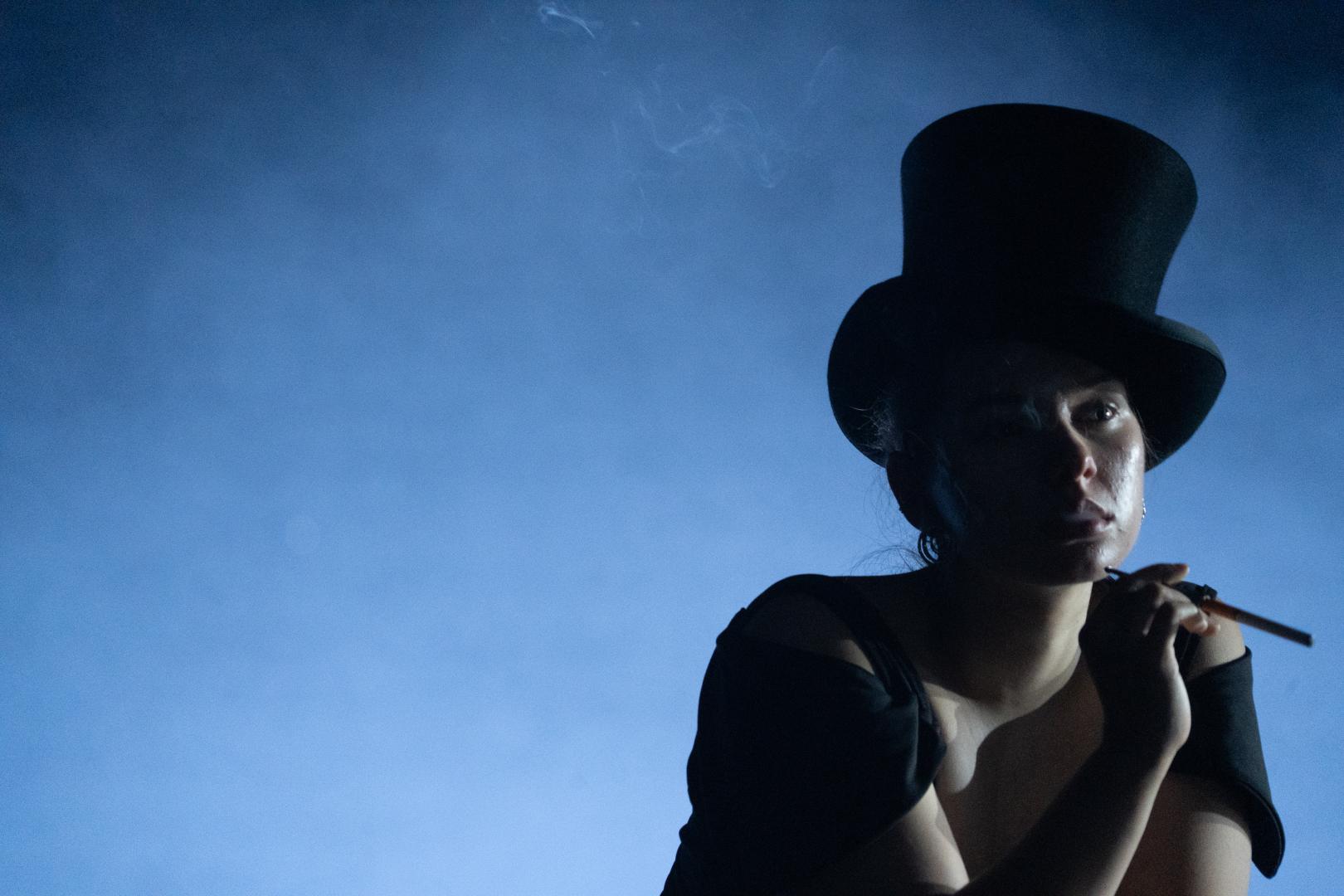 Eine Person trägt einen Hut und raucht eine Zigarette, der Hintergrund ist blau