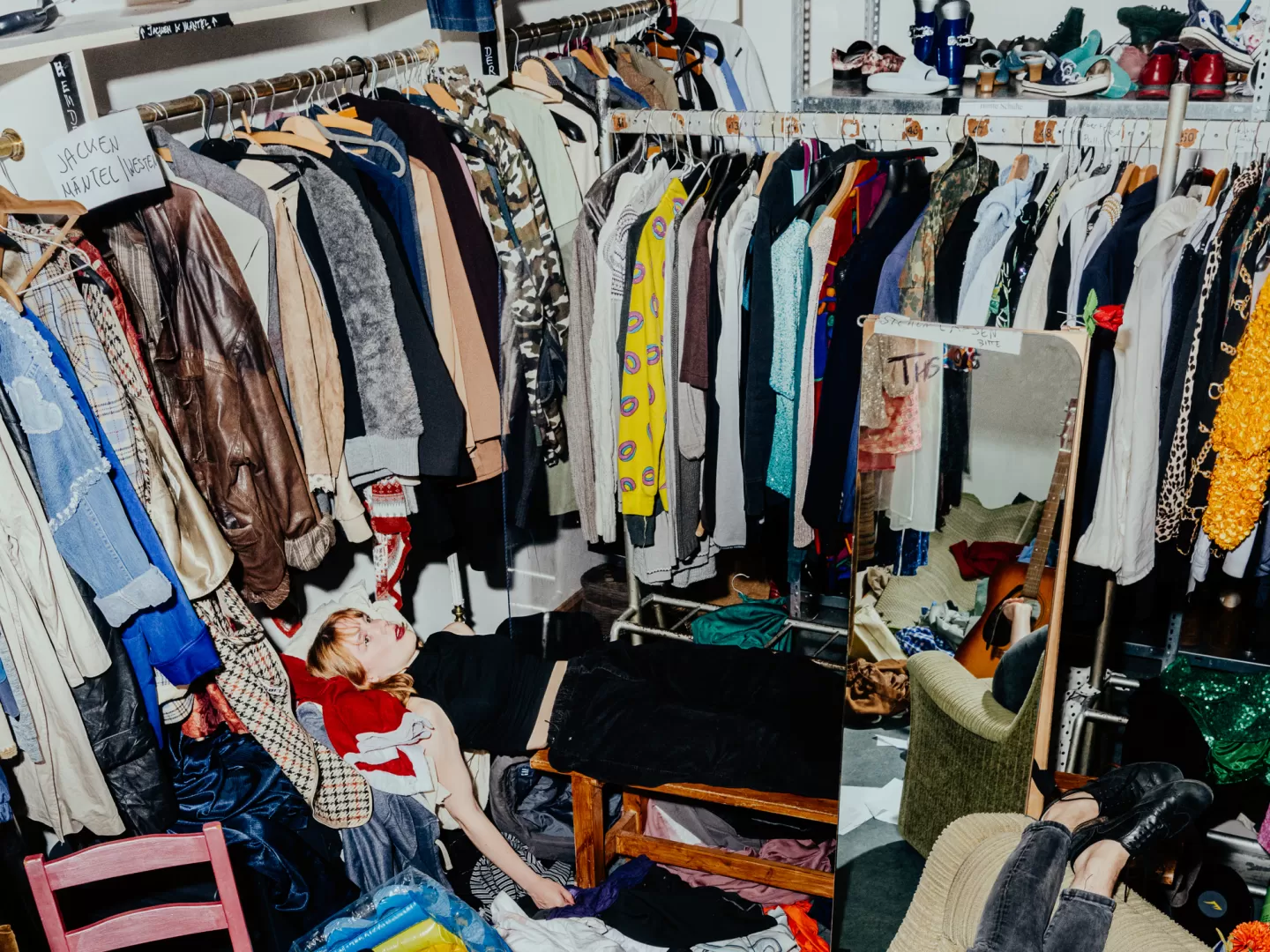 Eine junge Frau liegt im völlig chaotischen und überfüllten Fundus zwischen Kleidung und Gegenständen