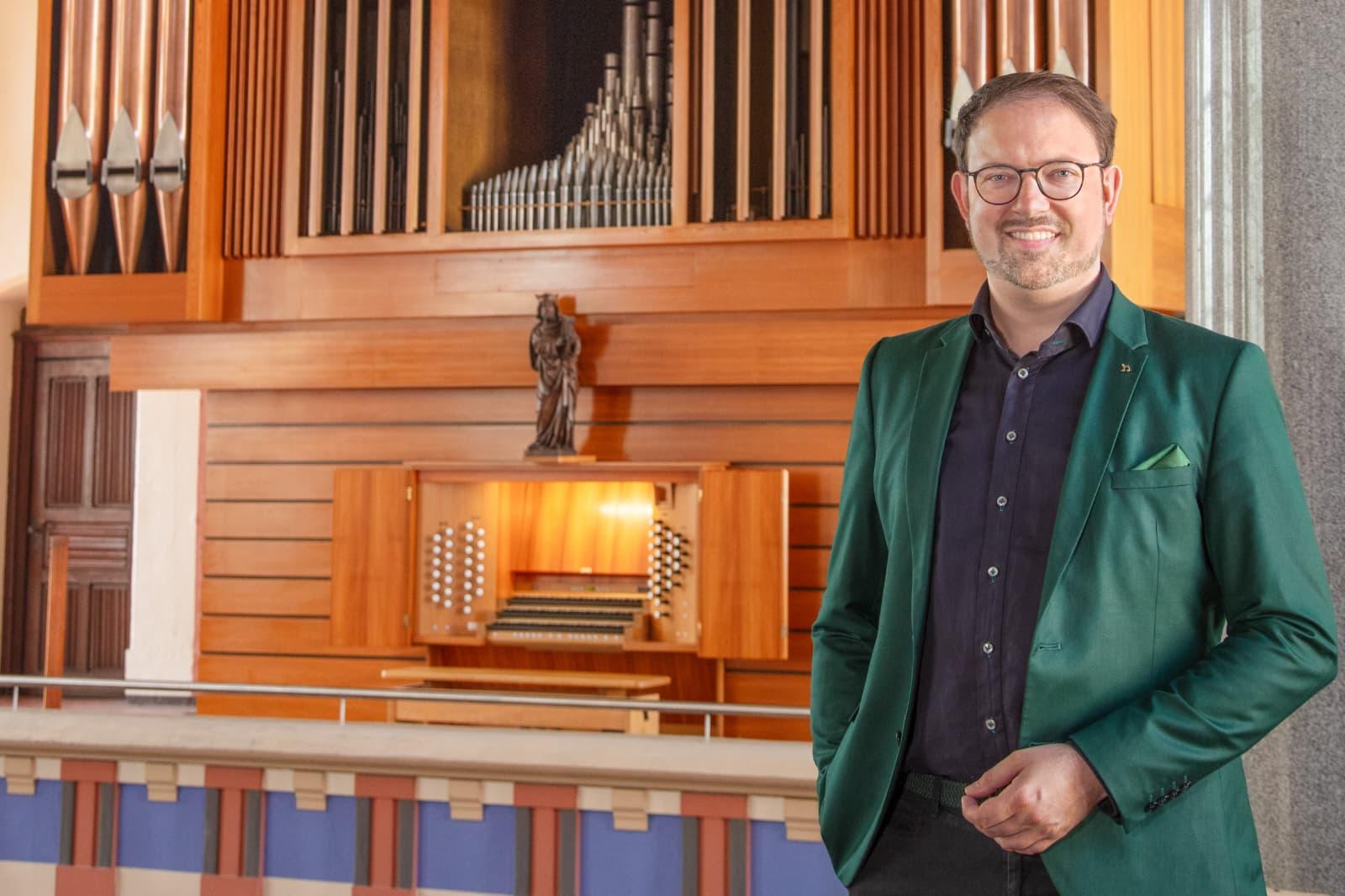 Simon Schumacher steht mit türkisem Jackett vor Orgel und lächelt in die Kamera