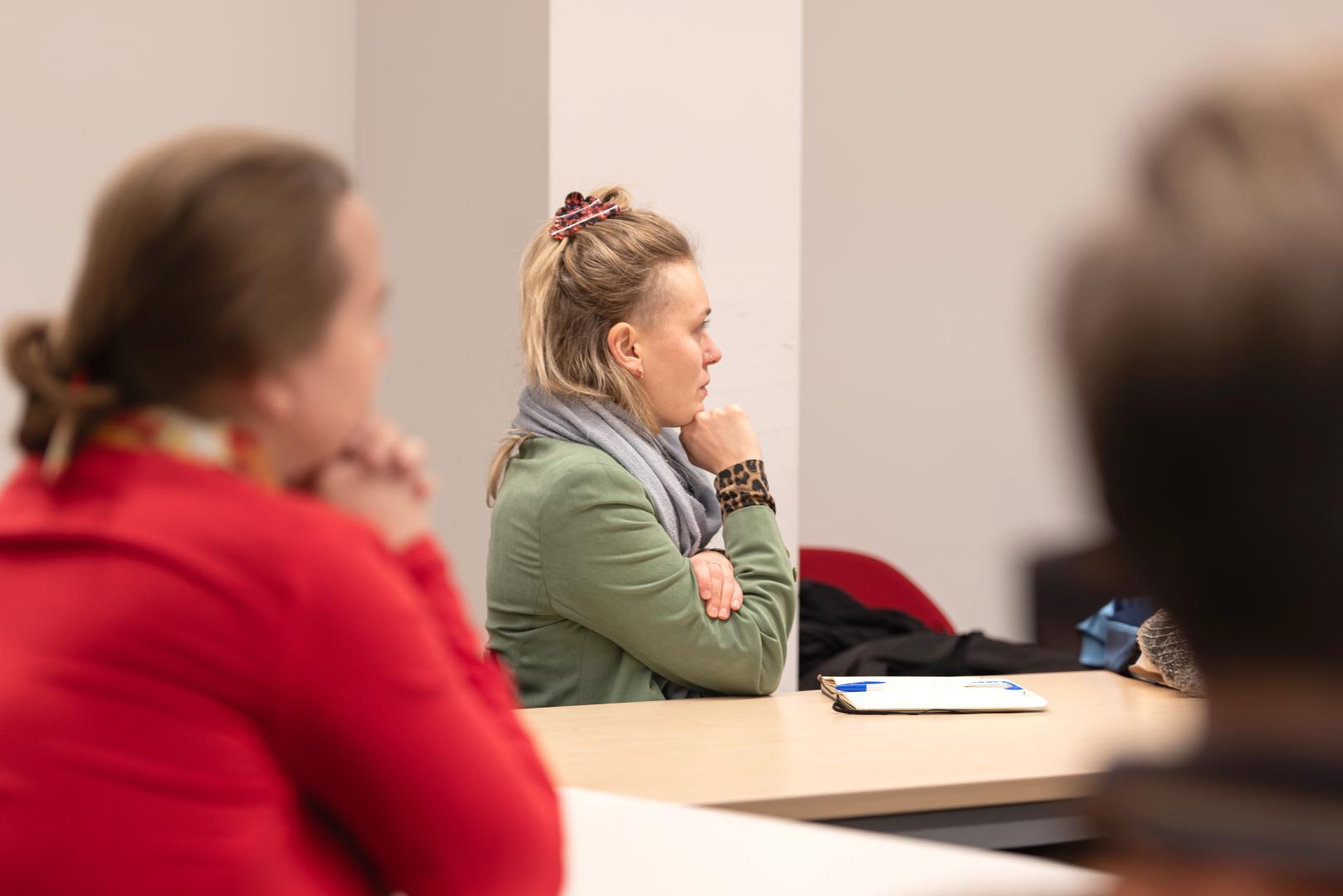 Drei Personen an einem Konferenztisch, die nach rechts blicken und einem Vortrag zuhören.
