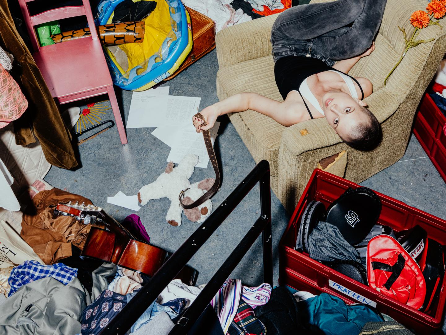 Eine junge Frau liegt auf einem Sessel im völlig chaotischen und überfüllten Fundus