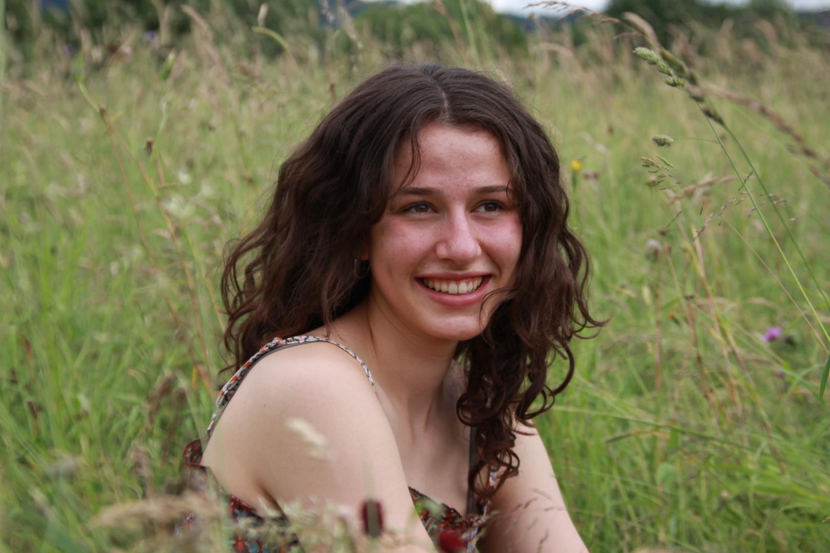 Junge Frau, die lächelnd auf einer Wiese sitzt.