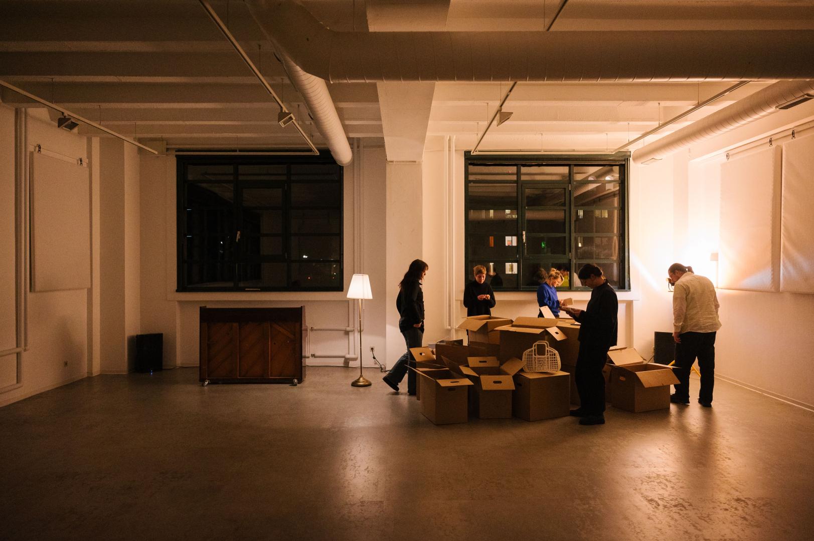 Leerer Raum, in dem Umzugskartons liegen, um die herum fünf Personen stehen.