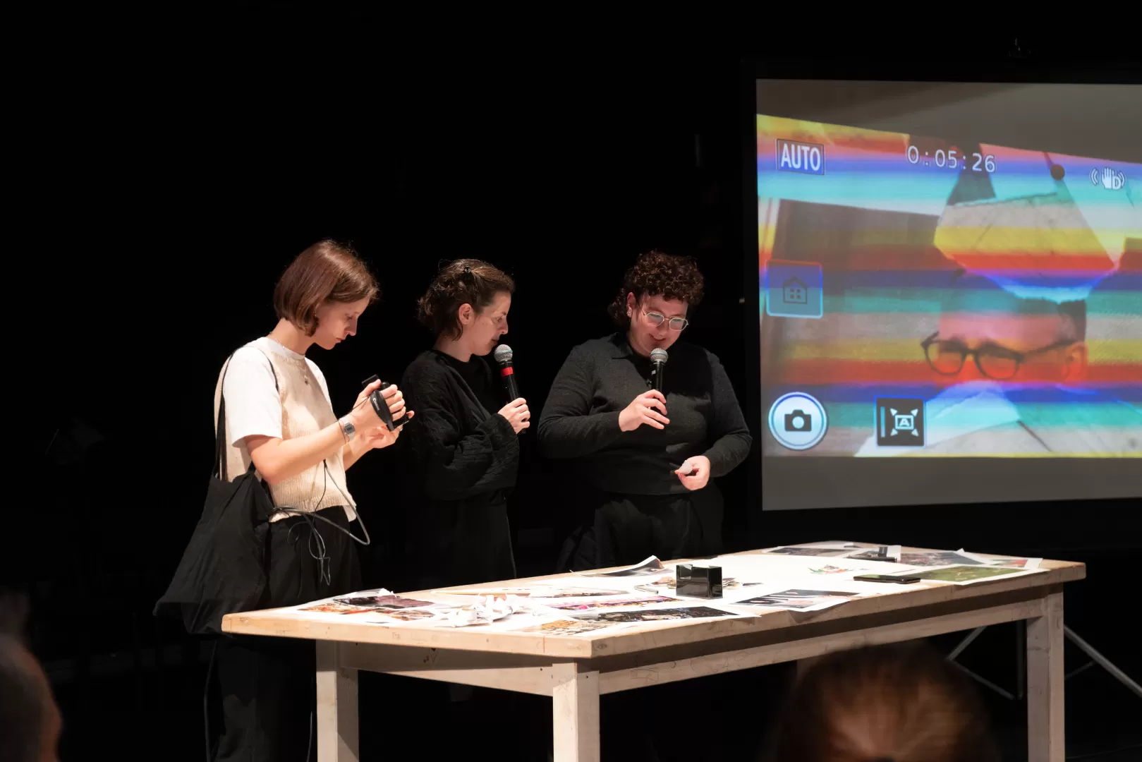 Drei Personen stehen an einem Tisch mit ausgedruckten Bildern.