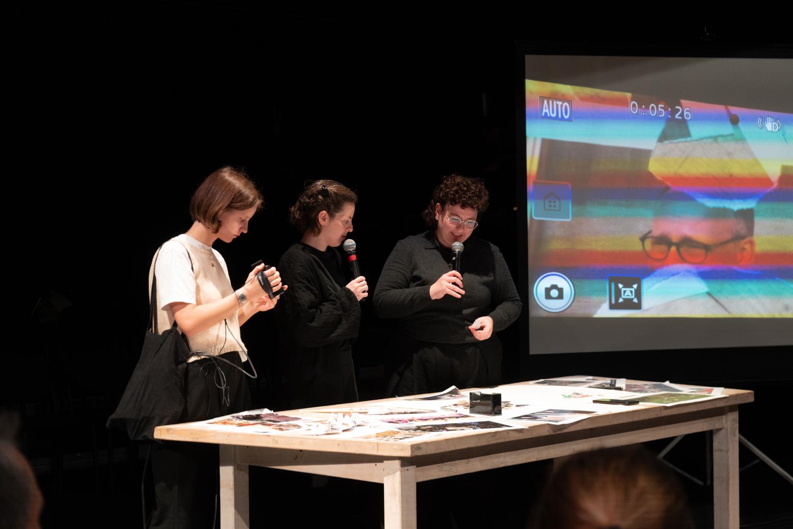 Drei Personen stehen an einem Tisch mit ausgedruckten Bildern.