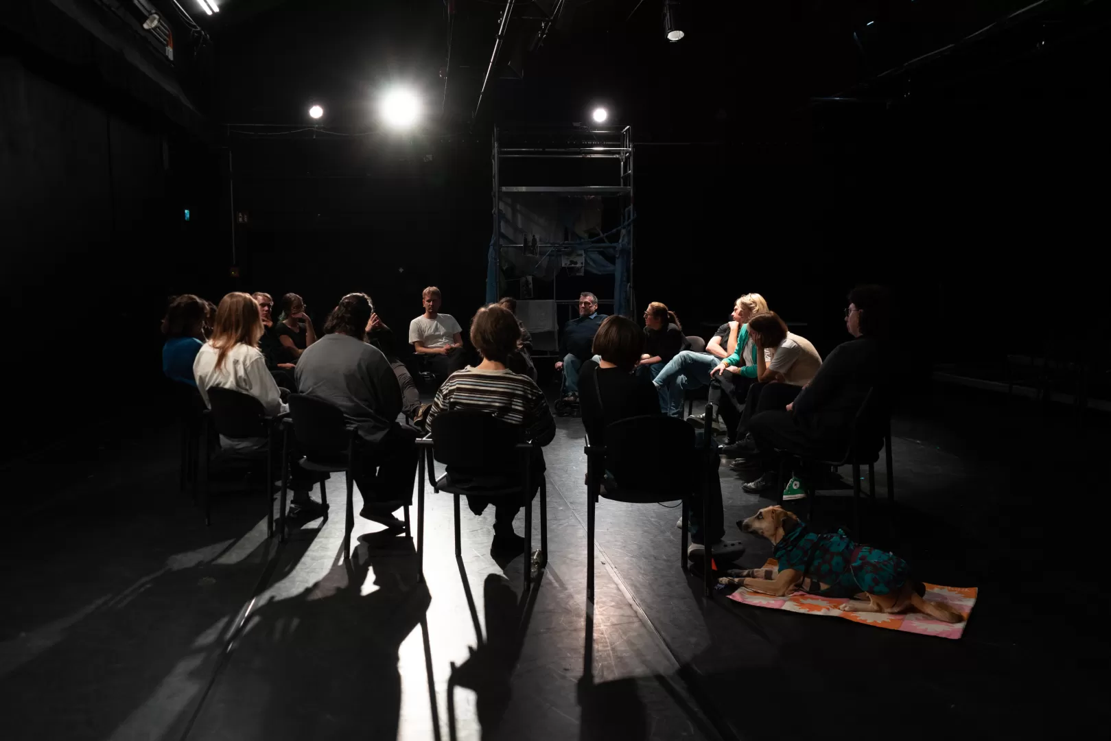Personen sitzen in einem Stuhlkreis auf einer Bühnenfläche.