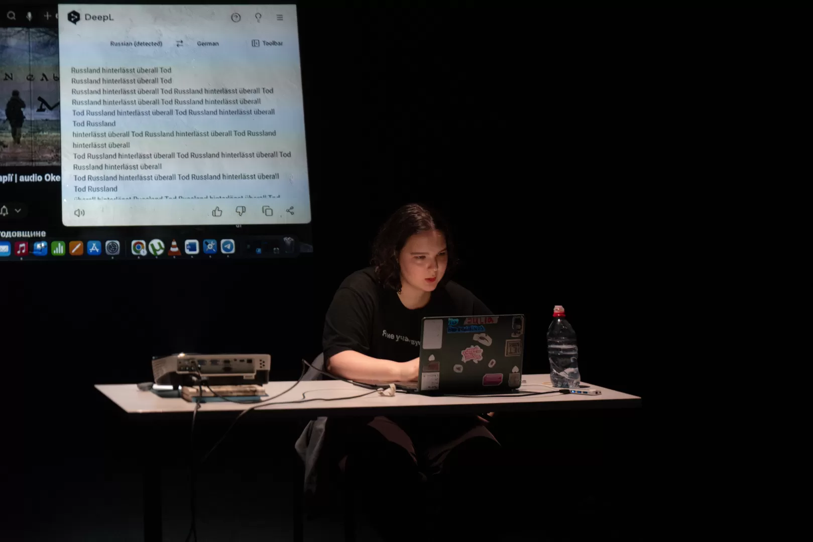 Eine Person sitzt mit Laptop an einem Schreibtisch, hinter ihr die Videoprojektion einer Google-Suche.