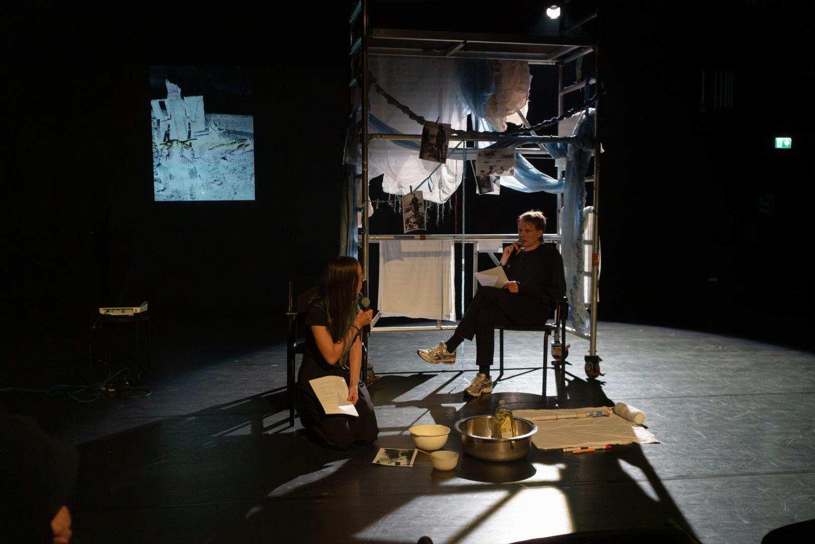 Zwei Personen vor einem Gerüst, dass mit Stoffen behangen ist.