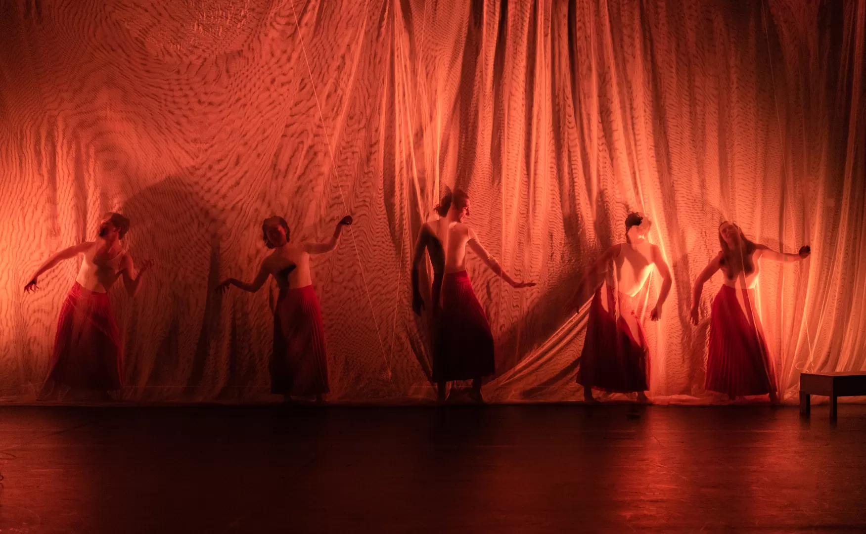 Personen in tanzenden Positionen hinter einem transparenten Vorhang.