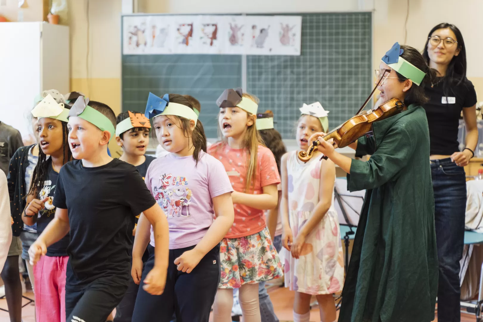 Schüler*innen bewegen sich zur Musik, die von einer Geigerin im Klassenraum gespielt wird.