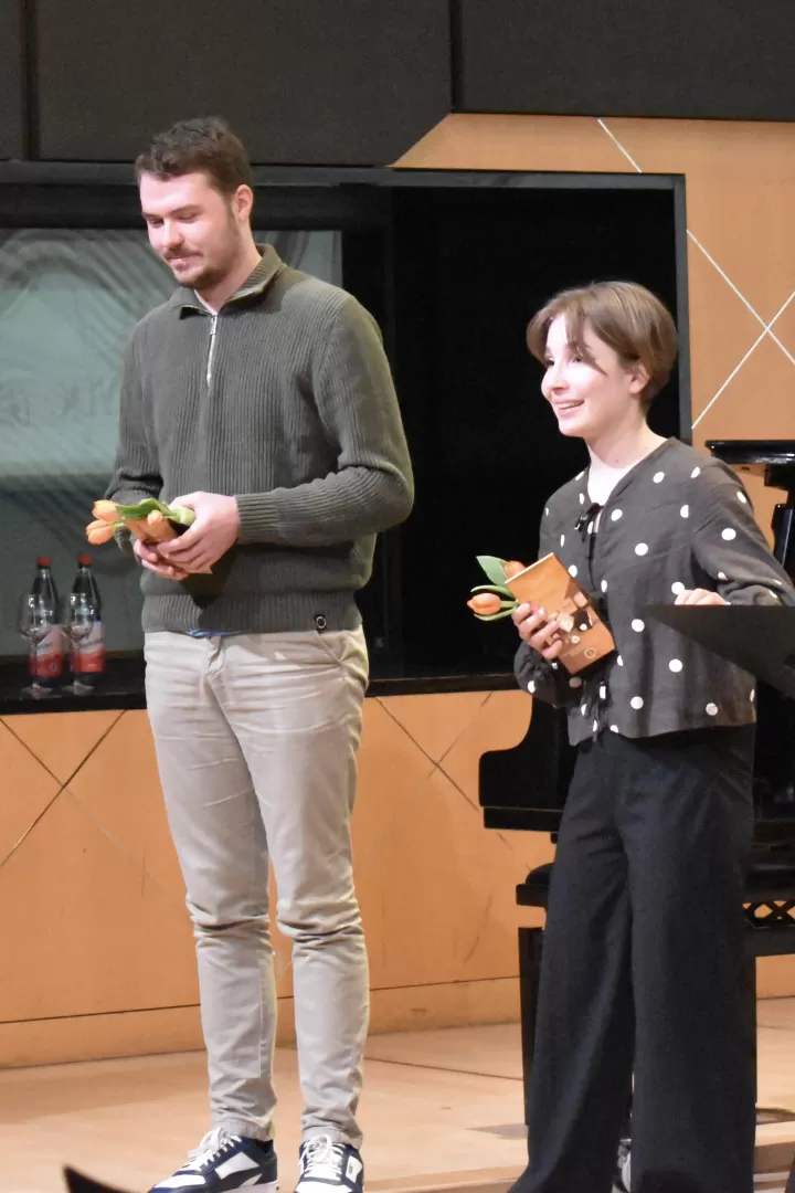 Zwei Musiker*innen stehen vor einem Flügel, mit Blumen und kleinen Geschenken in den Händen.