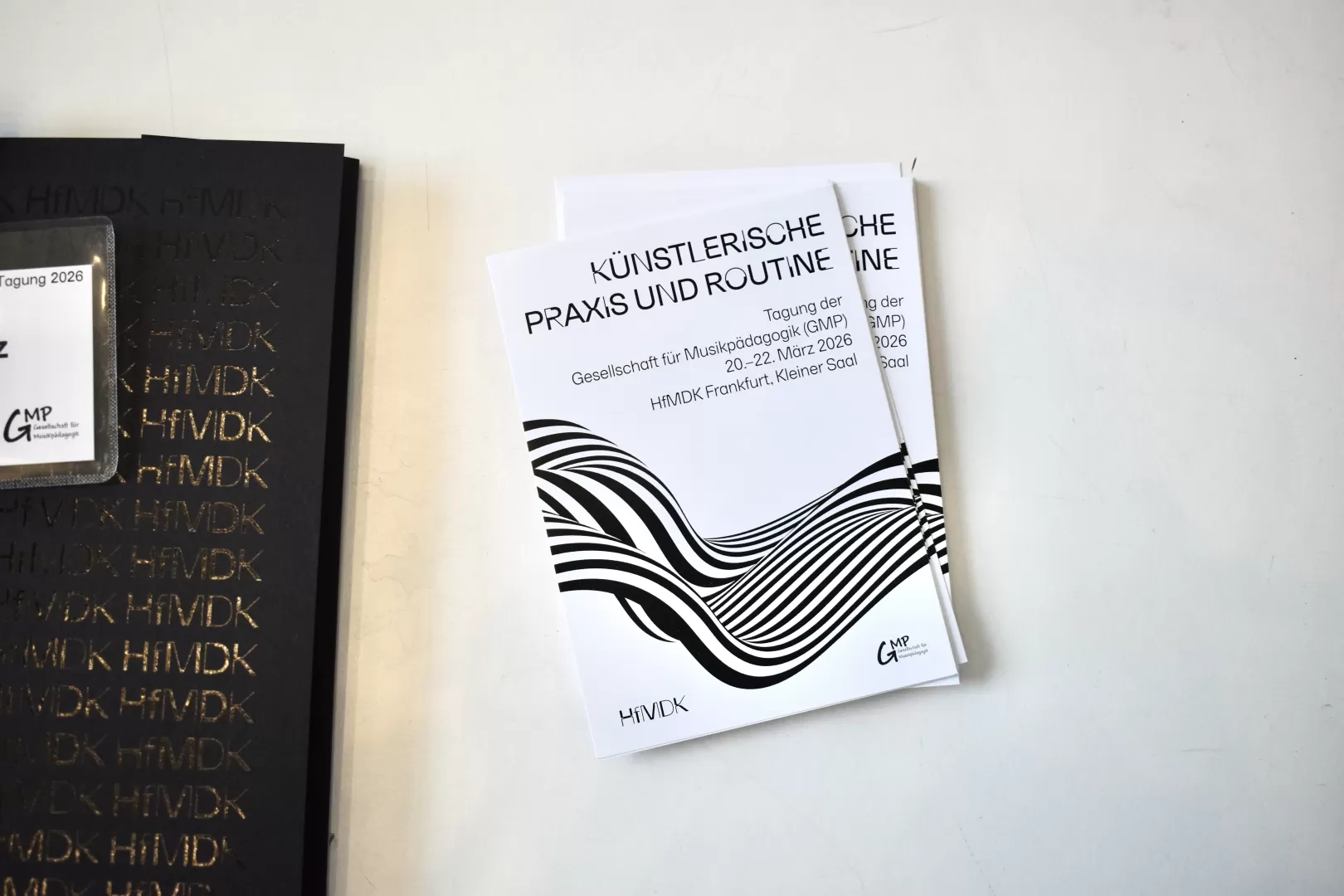Postkarten zur Bewerbung der Tagung liegen in einem Stapel auf einem Tisch, daneben eine Mappe mit den Logos der GMP und der HfMDK.
