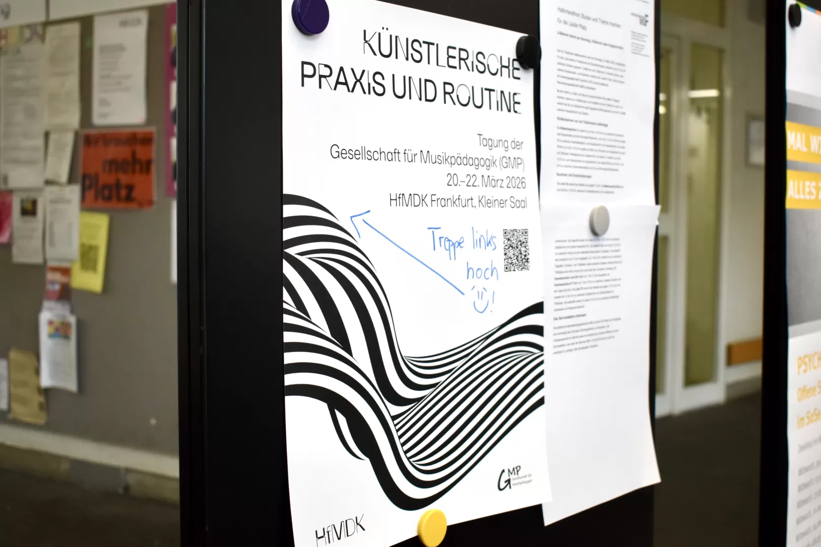 Ein Plakat an einer Magnetwand, das auf die Tagung der Gesellschaft für Musikpädagogik hinweist, mit einer handschriftlich notierten Wegweisung.