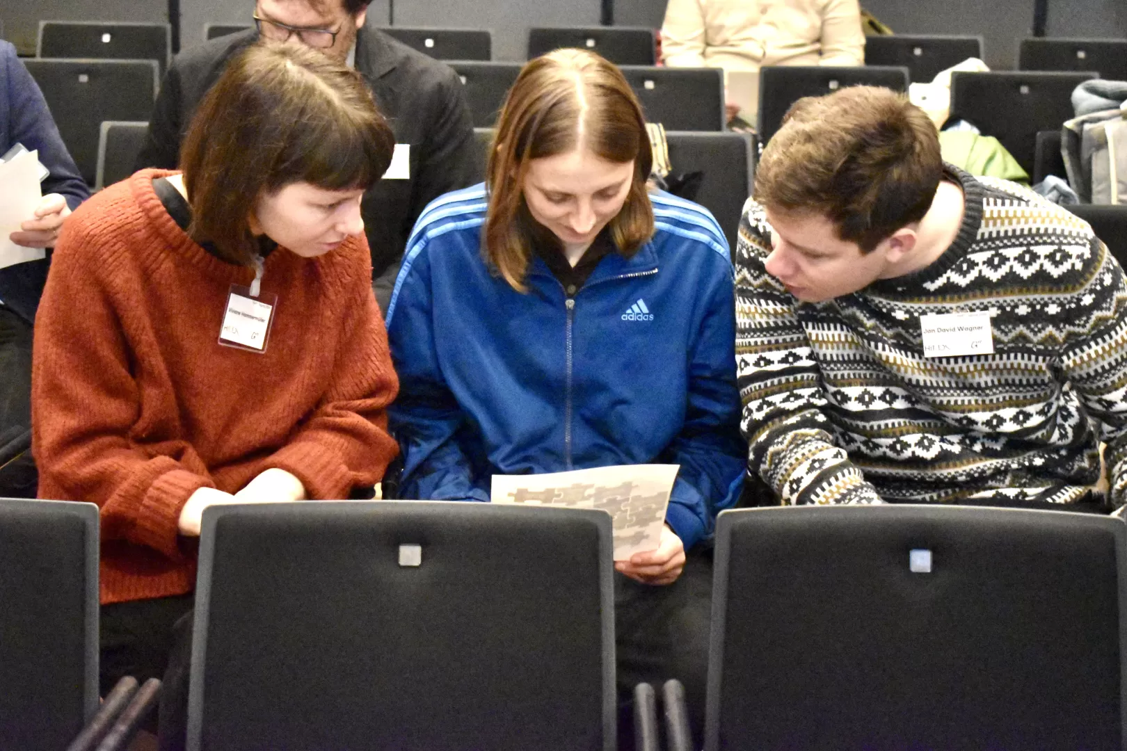 Drei Personen sitzen in einer Stuhlreihe und besprechen gemeinsam ein Arbeitsblatt.