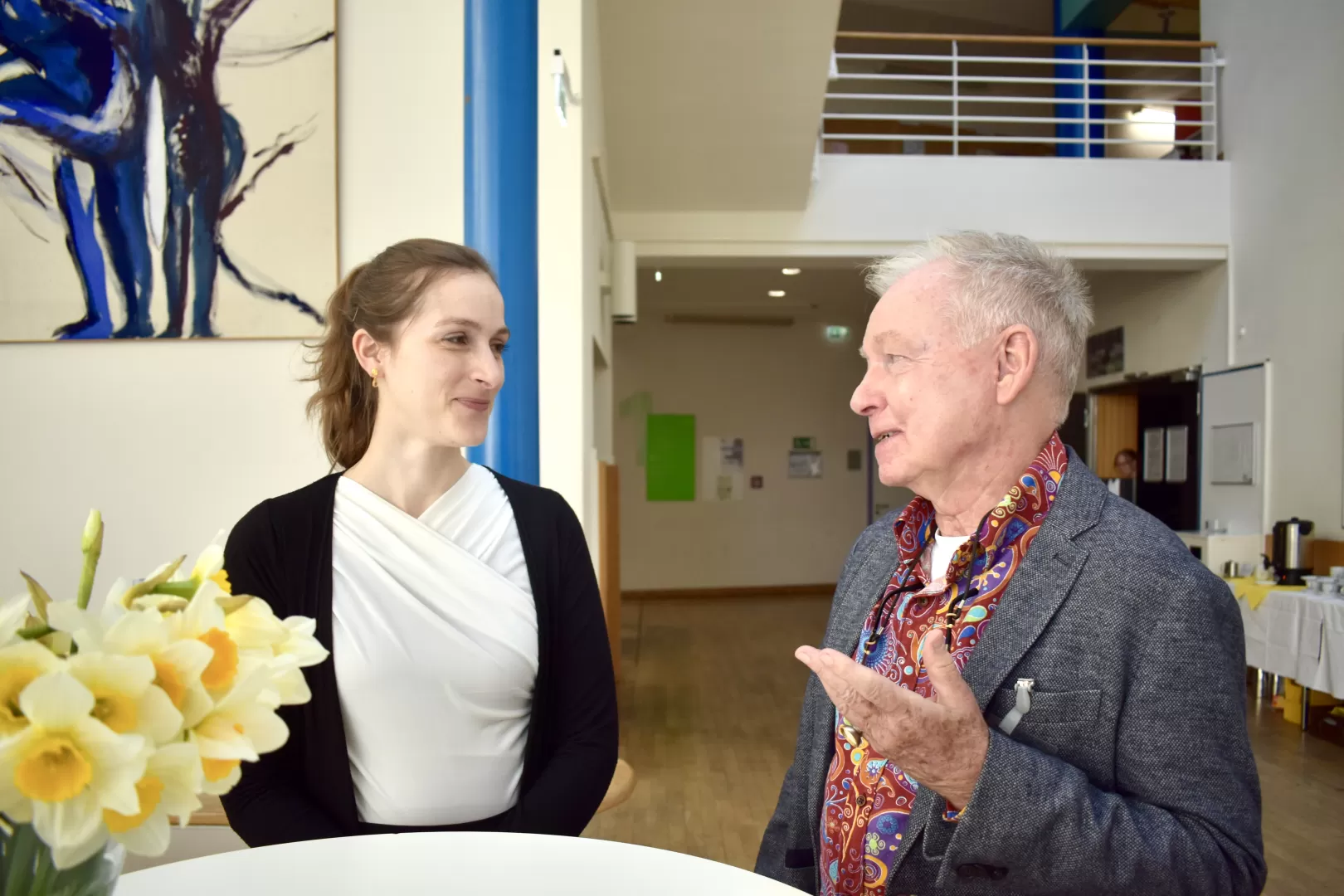 Lea Tigger und Peter W. Schatt diskutieren an einem Stehtisch im Foyer der HfMDK miteinander.