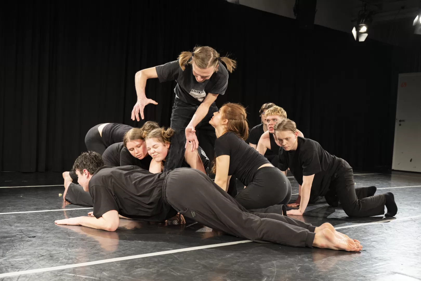 Acht Schauspielstudierende in schwarzen Klamotten krabbeln auf dem Boden