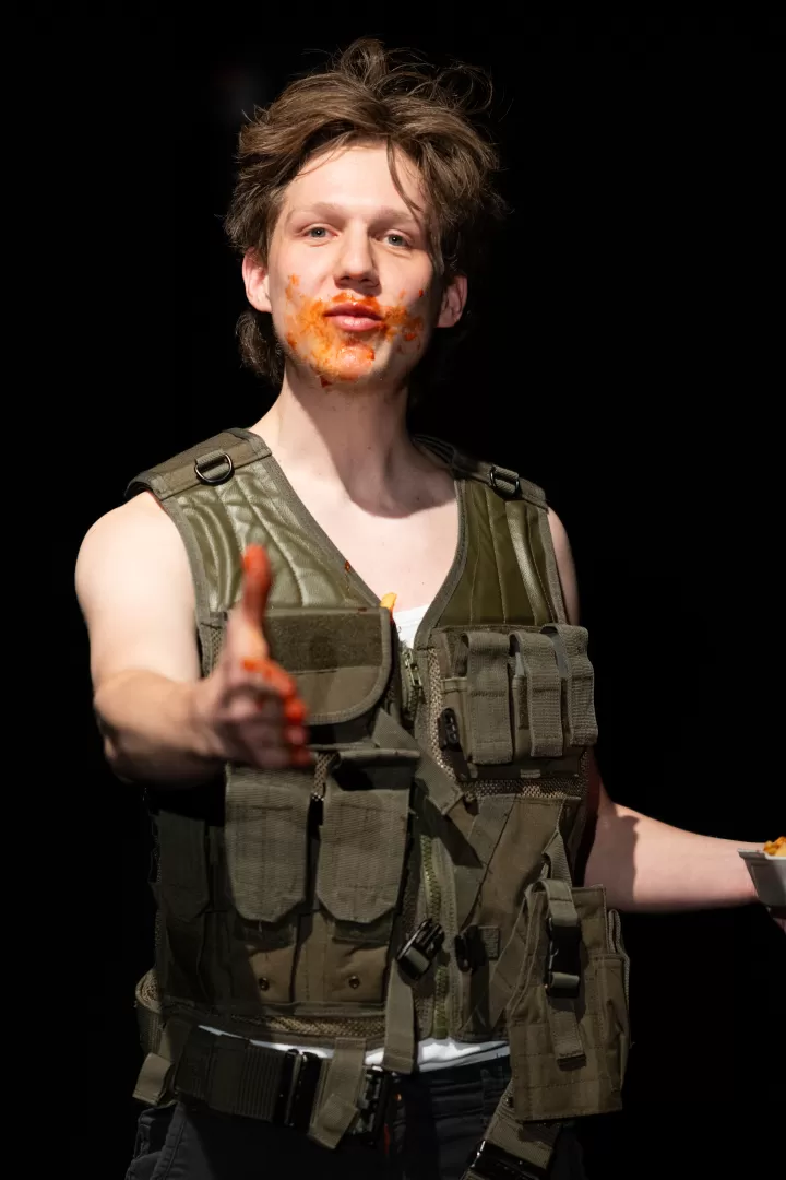 Mann mit Militärweste und mit Ketchup verschmiertem Gesicht streckt die Hand zur Begrüßung aus.