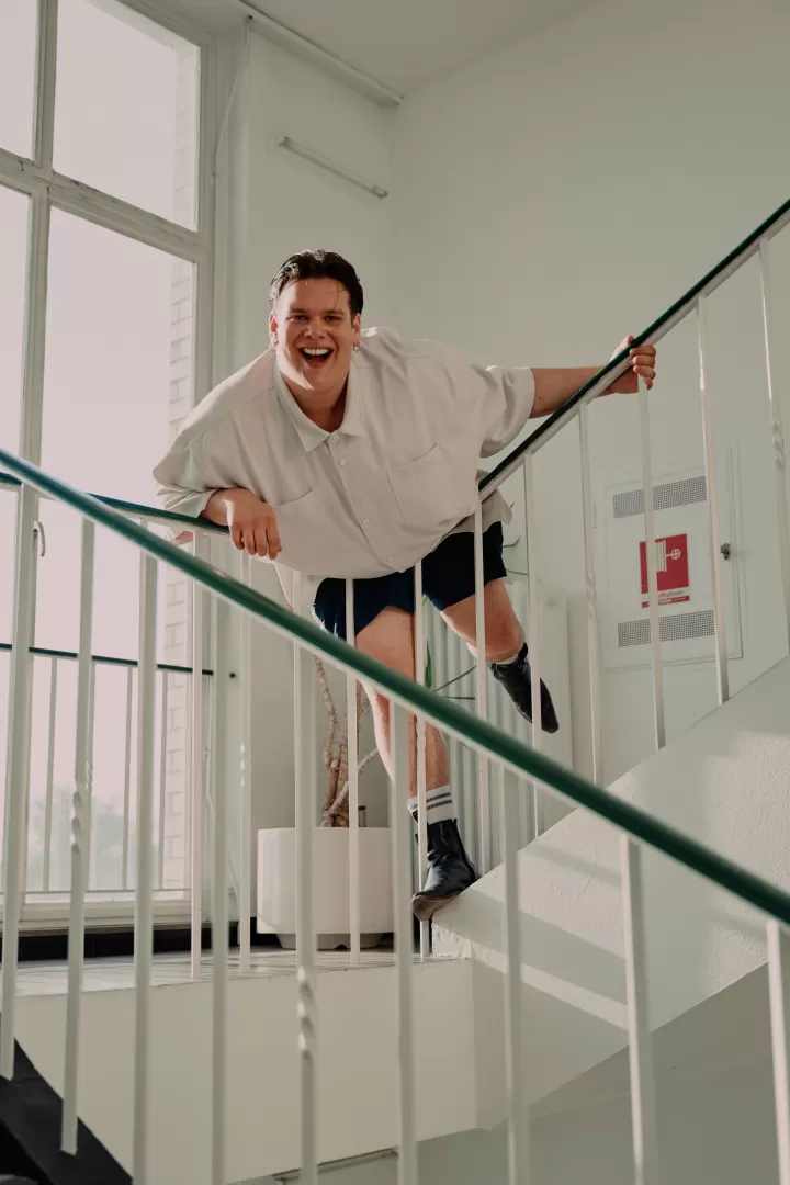 Mann auf einer Treppe lehnt sich weit über das Gelände und lacht.