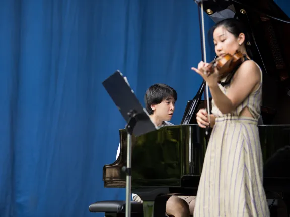 Ein Pianist und eine Geigerin vor einem blauen Hintergrund