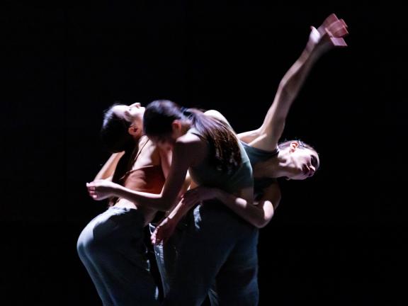 Drei Tänzerinnen in schneller Bewegung, die Körper ineinander verschlungen.