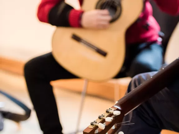 Unterricht im Fach Gitarre, im Vordergrund die Gitarre des Dozenten, im Hintergrund spielt der Student.