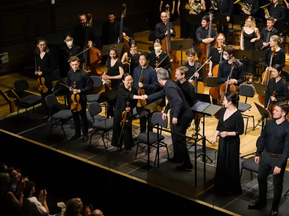 Der Dirigent schüttelt der Konzertmeisterin nach einem Konzert von Chor und Orchester auf der Bühne des Großen Saals die Hand.