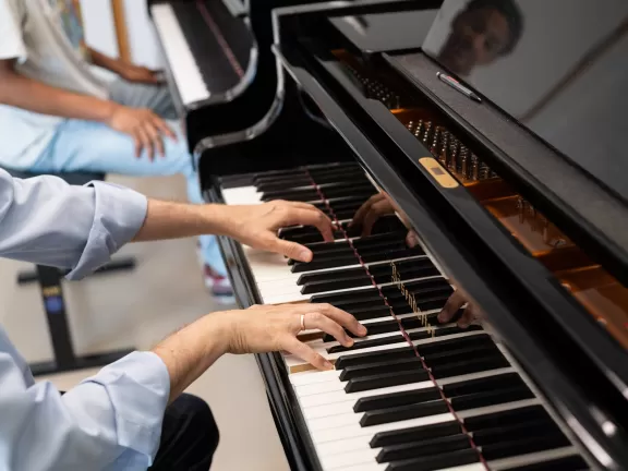 Klavier-Einzelunterricht: Nahaufnahme der Hände des Professors, der am Klavier dem Studenten etwas vorspielt.