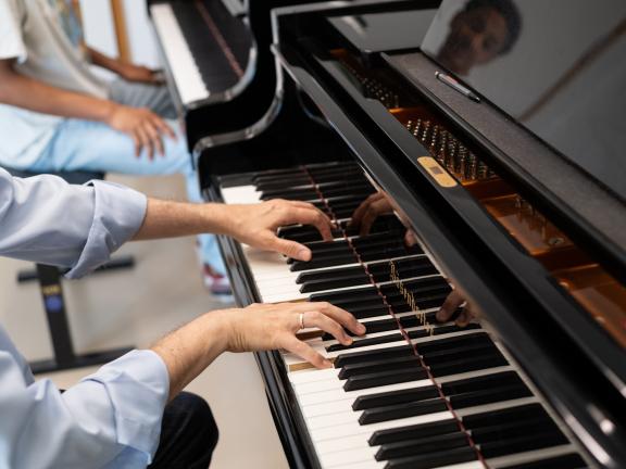 Klavier-Einzelunterricht: Nahaufnahme der Hände des Professors, der am Klavier dem Studenten etwas vorspielt.