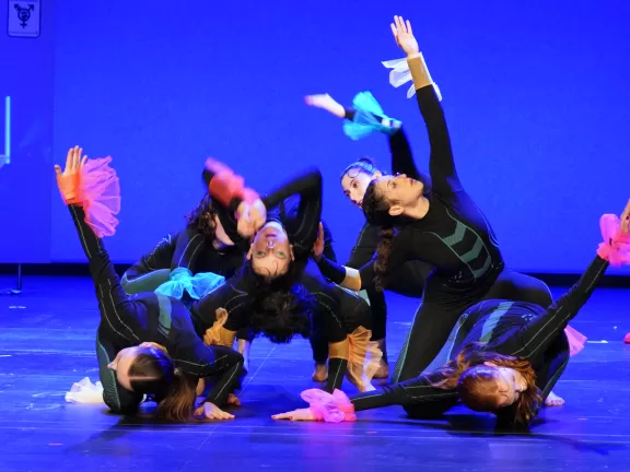 Gruppenfoto mit Performer*innen, die in schwarzen engen Anzügen vor einer dunkelblauen Bühne posieren