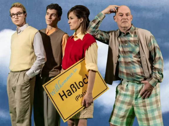 Vier Menschen stehen hinter blauem Hintegrunnd und halten ein Ortsschild