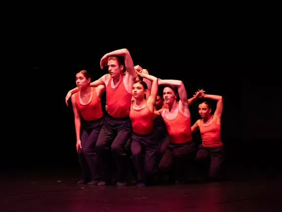 Szene aus einer Tanzperformance, eine Gruppe Tänzer*innen in rotes Bühnenlicht getaucht.