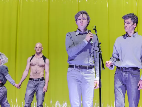 Vier Menschen stehen vor einer gelben Wand, sie sind grau angezogen.