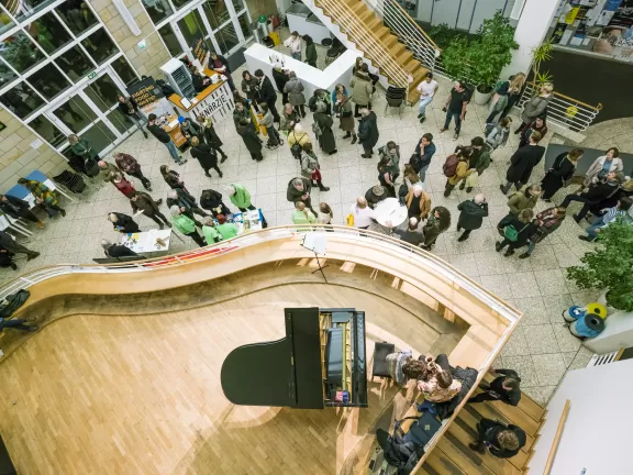Das Foyer von oben: Man sieht einen Flügel auf der Empore und viele sich unterhaltende Menschen im Foyer.