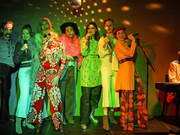 "The winner takes it all" ABBA-Liederabend Studiojahr Schauspiel Acht Leute in bunter Kleidung singen auf einer Bühne