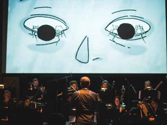 Musik für Stummfilme Dirigient vor einem Ensemble, im Hintergrund eine Leinwand auf der ein Stummfilm