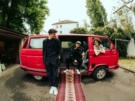 Drei Männer in einem roten Kleintransporter