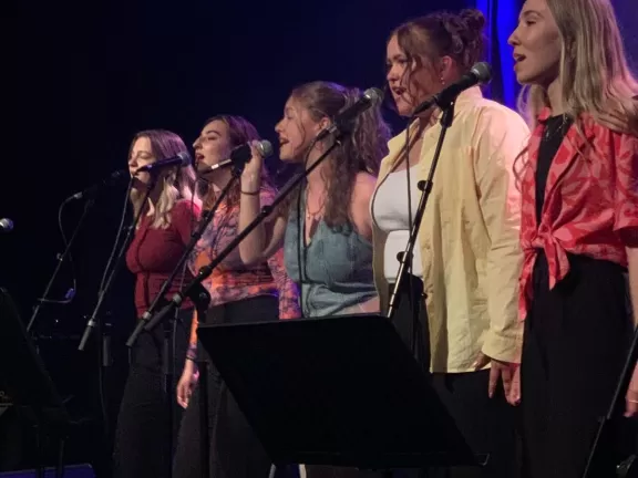 Fünf Frauen singend hinter Mikros auf einer Bühne