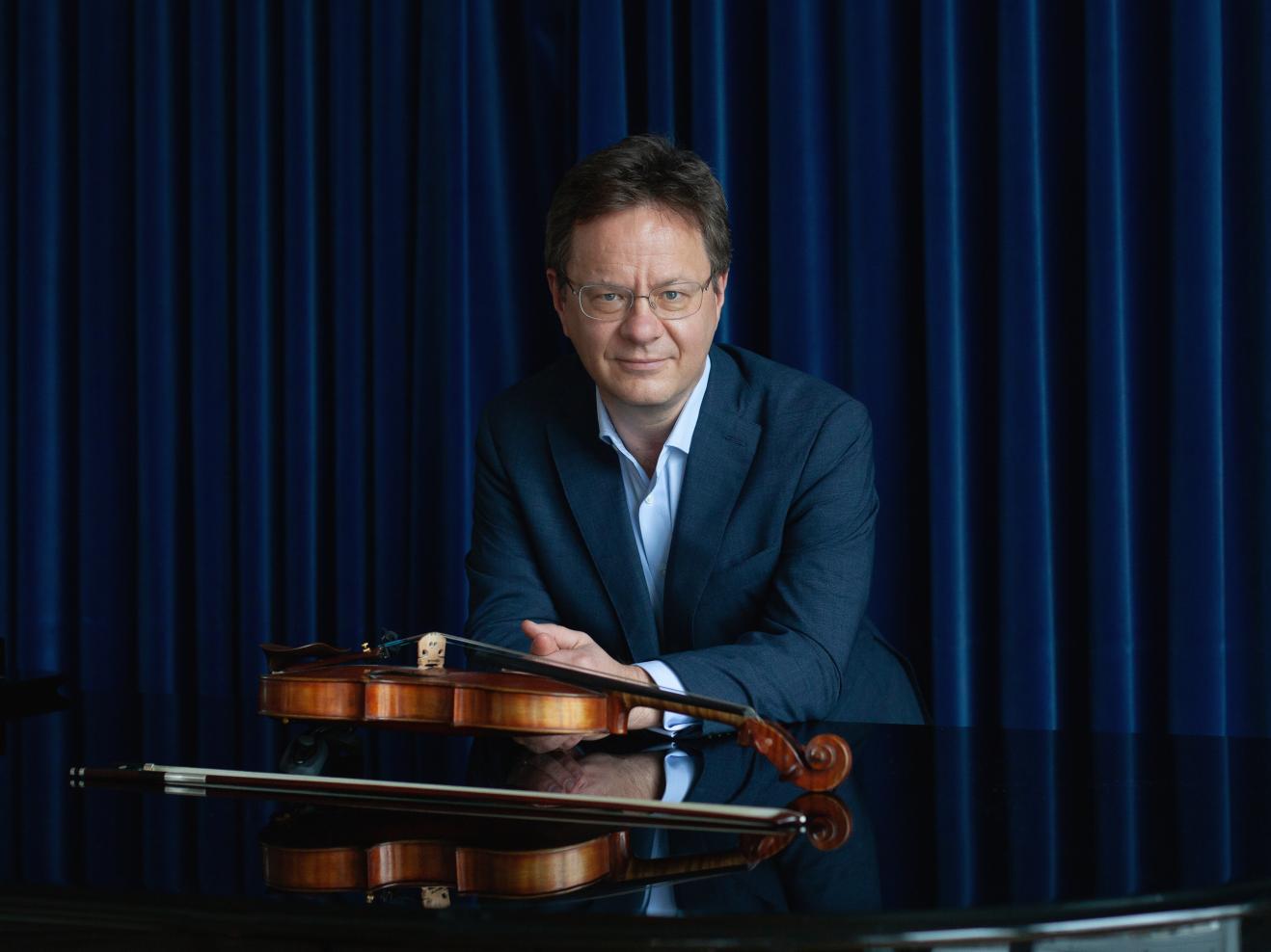 Porträt von Prof. Tim Vogler mit Geige vor einem blauen Vorhang