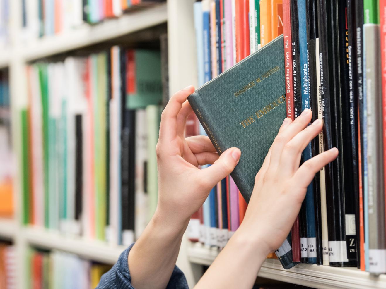 Eine Person zieht ein Buch aus einem Bücherregal.