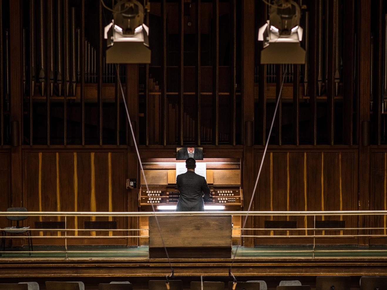 Rückansicht eines Organisten an der Orgel, aus der Ferne betrachtet.