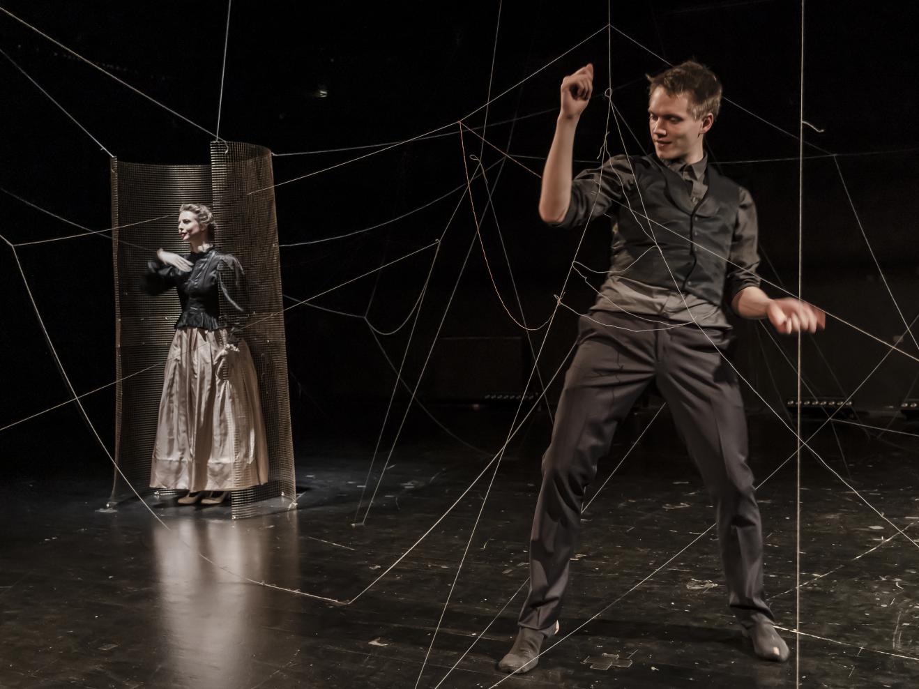 Eine Schauspielerin und ein Schauspieler, von Schnüren in einem Netz gefangen auf der Bühne des Frankfurt LAB