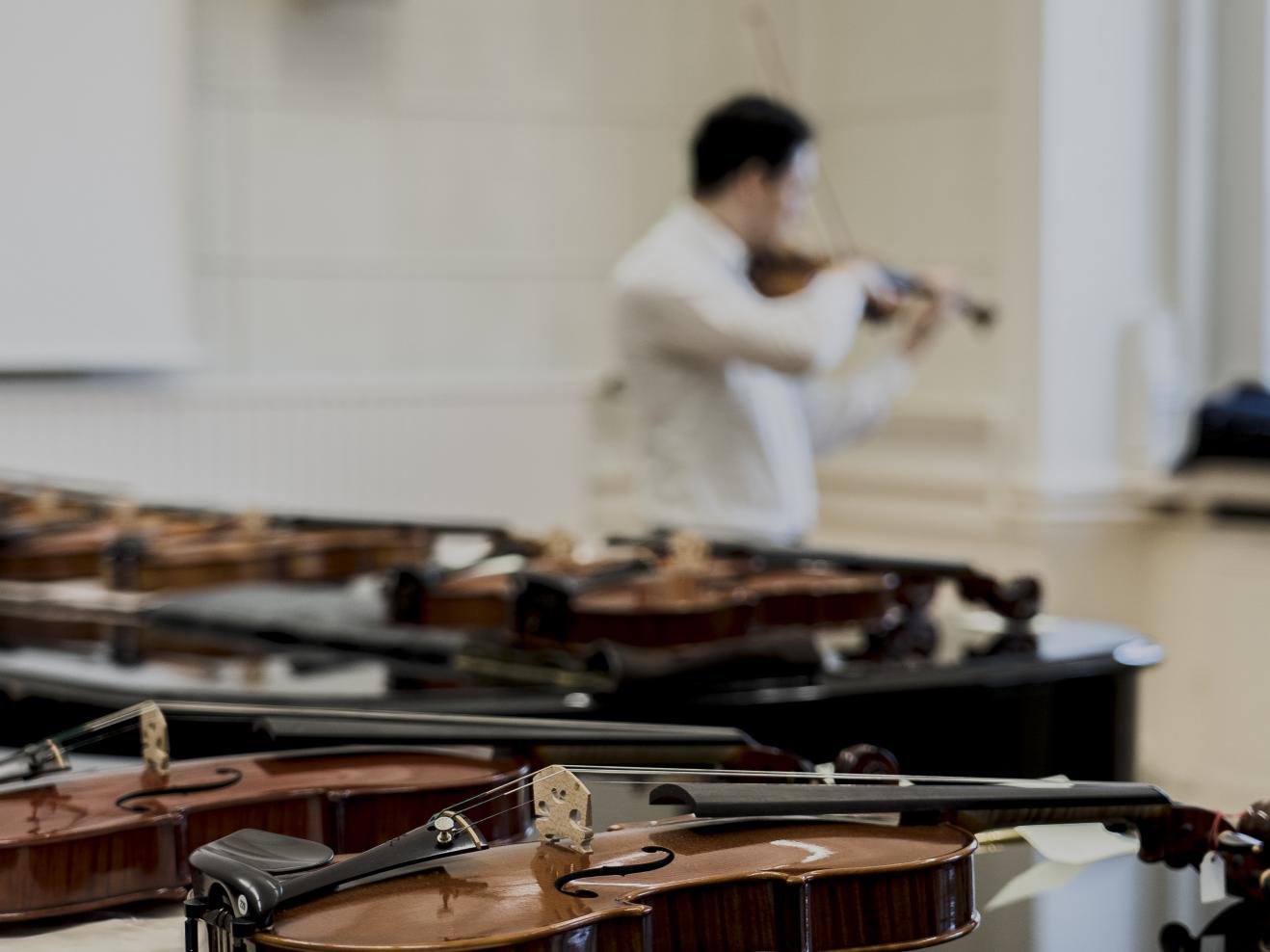 Geigen im Vordergrund, Prof. Erik Schumann spielt im Hintergrund auf einer Meistergeige