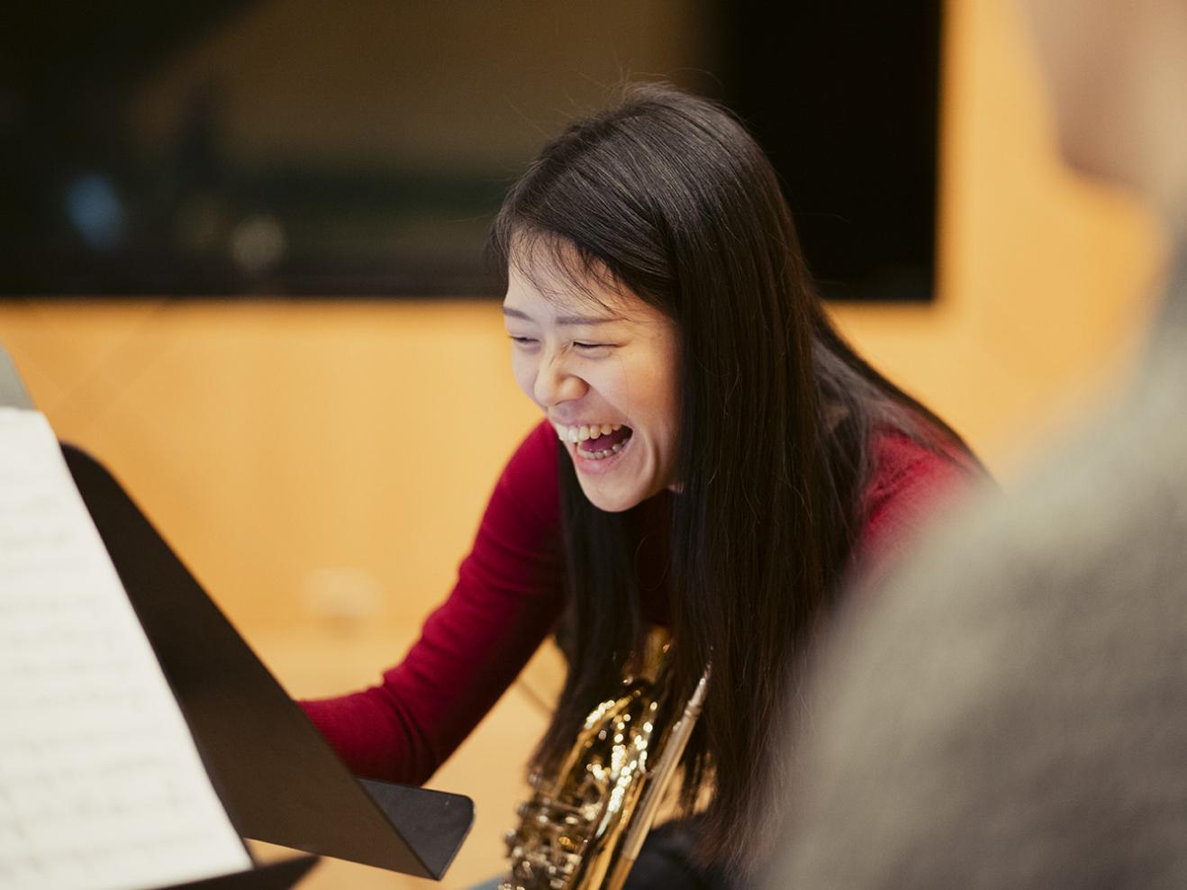 Eine Hornistin mit ihrem Instrument macht sich eine Notiz und lacht. 