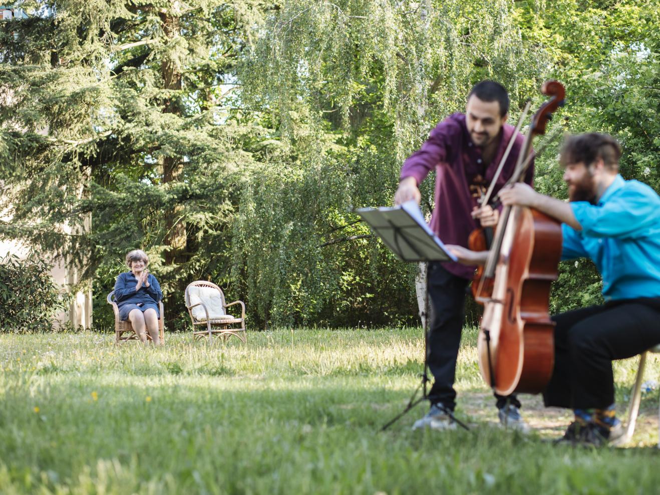 Zwei Musiker im Garten, eine Frau sitzt einige Meter weg und klatscht